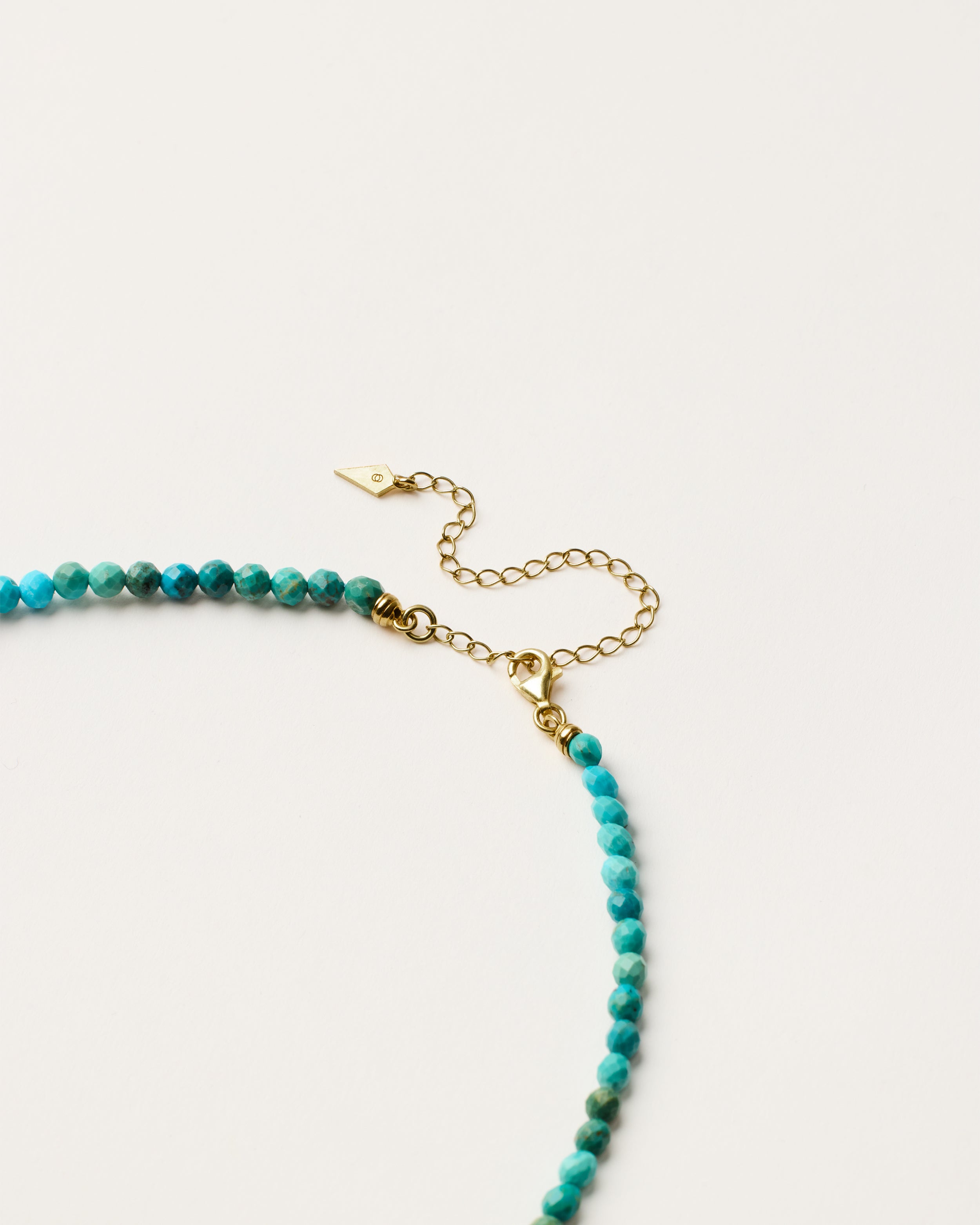 ENCARA AZURA Turquoise necklace with raw polished quartz point pendant, gold 8 cm extension chain and clasp, arrowhead-shaped fantasy signature, and 4 mm faceted turquoise bead strand.